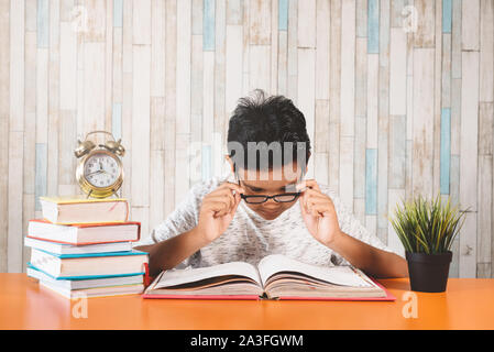 Young teenage reading books while fixing his spectales for focus. Concept of education, student, vision and hardworking Stock Photo