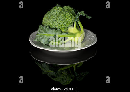 One whole fresh green broccoli on white plate isolated on black glass Stock Photo