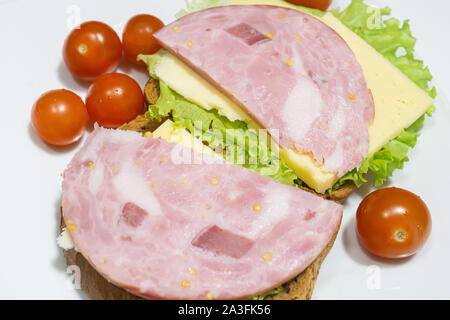 Tasty sandwich. slices of fresh bread with dried pork ham, green salad leaves and cherry tomatoes on white plate. isolated on white. Stock Photo