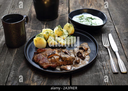 Grilled pork steak baked with mushrooms and cheese, served with potatoes and cucumber salad. Stock Photo