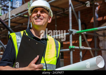 Male builder foreman, worker, contractor or architect on construction site holding black clipboard and archtectural plans Stock Photo