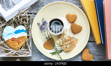 Heart shaped cookies and handmade painted gingerbread in a present box; coffee, lavender, shell and books  are nearby on wooden table, flat lay, top v Stock Photo