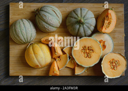 Heads of cantaloupe and pieces of melon of different shapes on the wooden surface.Rustic style.Flat lay. Stock Photo