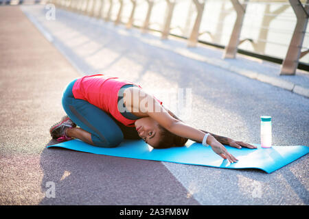 Dark-skinned woman doing yoga on sport mat near water bottle Stock Photo