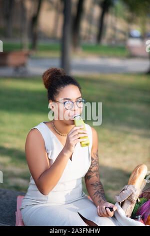 Dark-haired woman wearing glasses drinking yummy juice Stock Photo