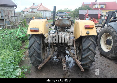 Yellow tractor without a cab in the courtyard of a dairy farm. View from the back. Apartment building in the background. Podlasie, Poland. Stock Photo