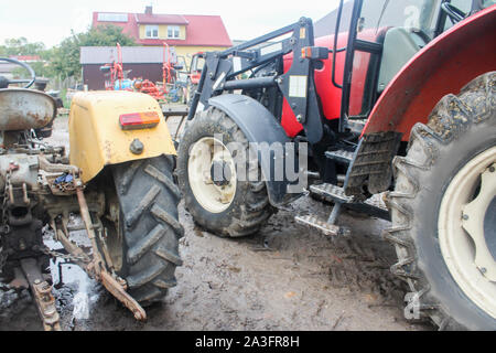 Yellow and red tractors  in the courtyard of a dairy farm. View from the back. Apartment building in the background. Podlasie, Poland. Stock Photo