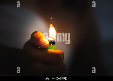close up of a hand holding a lighter in the dark and starting fire Stock Photo