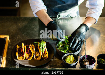 A chef plating tacos in a restaurant kitchen Stock Photo