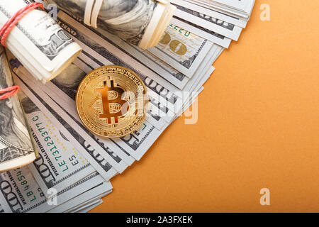 Golden Bitcoin coin on a us dollars close up on the orange background with copy space.