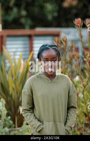 Pretty smiling black girl in a polka-dot hoodie by tall plants Stock Photo