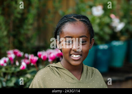 Beautiful smiling black girl in polka-dot shirt with flowers & plants Stock Photo