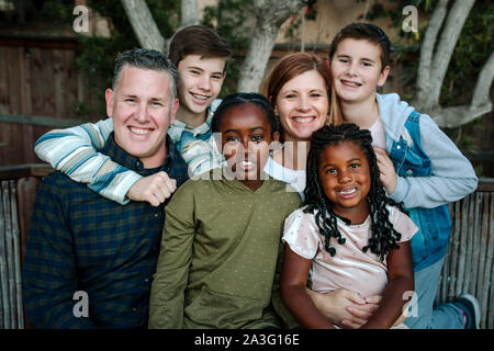 Hugging happy multiracial family smiling in front of tree Stock Photo