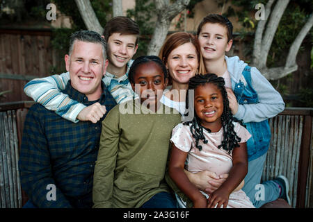 Smiling happy multiracial family hugging in front of tree Stock Photo