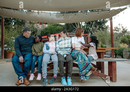 Multiracial family relaxing on a bench under a white sun canopy Stock Photo