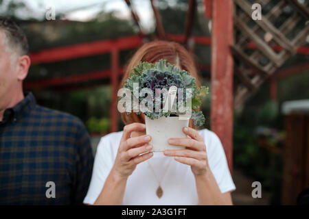 Red-haired woman wearing white shirt holding plant in front of face Stock Photo