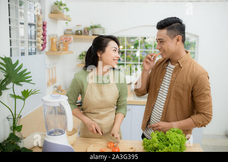 Beautiful young Asian couple is talking and smiling while cooking healthy food in kitchen at home Stock Photo