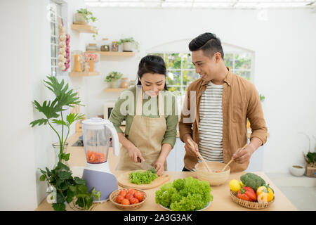 Smiling young Asian couple cooking food in the kitchen