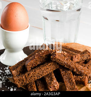 Healthy food. A boiled egg in a white ceramic stand stands on a wooden table next to rye croutons and white sauce Stock Photo