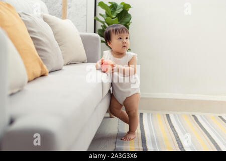 Lovely standing baby next to the sofa. Cute portrait of happy face baby girl Stock Photo