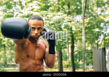 Young sweated boxer performing shadow boxing on the sports ground outdoors Stock Photo