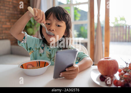 distracted kid using mobile phone while having breakfast on the table Stock Photo