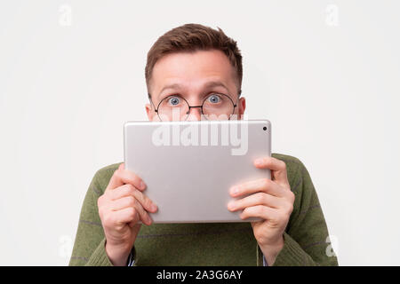 Young guy in funny glasses hiding his face with e-book reader Stock Photo