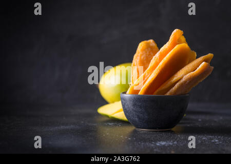 Fresh and dried mango chips on black background. Close up. Space for text. Stock Photo
