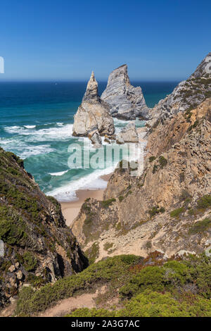 Scenic view of the Atlantic Ocean, rugged coastline with huge boulders and trail to the Praia da Ursa beach near Cabo da Roca in Sintra, Portugal.