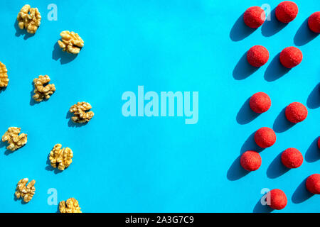 Walnuts and strawberry red candies on blue background with copy space. Flat lay, top view. Stock Photo