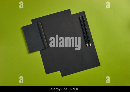 Two sheets of black paper, two pencils and folder on green background with copy space. Education, workplace concept. Top view in focus with different Stock Photo