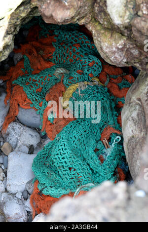 Green and orange fishing net washed up between rocks on Gower Stock Photo