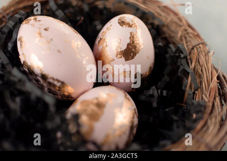 Painted and gold foiled easter eggs in a nest. Moody tones, top view. Idea of a modern easter celebration. Stock Photo