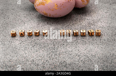 Painted eggs in rose gold and Happy easter letters on a grunge texture granite or concrete background. Dark moody tones. Idea of a modern easter holid Stock Photo