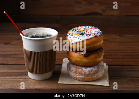 A paper cup of hot fresh brewed coffee next to a stack of fancy donuts. Stock Photo