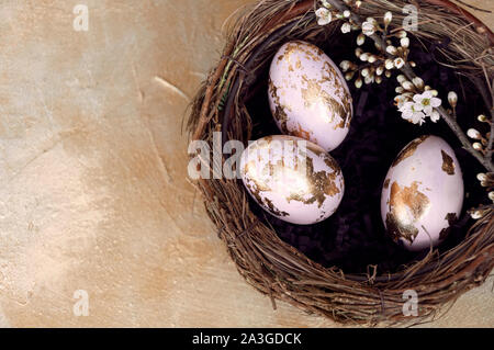 Gold foiled painted easter eggs in a nest, decorated with a cherry blossom branch. Top view, copy space for text. Stock Photo