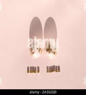 Easter bunny rabbit ears, made of gold foild eggs and its shade on a pale pink wooden background. Symbol of Easter holidays and spring time. Minimal c Stock Photo