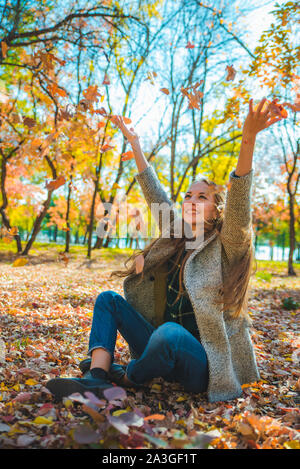 young pretty woman playing with yellow autumn leaves at city park Stock Photo