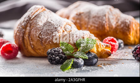 Freshly crispy croissants sprinkled sugar powder with raspberry blackberry and blueberry with mellisa leaves Stock Photo
