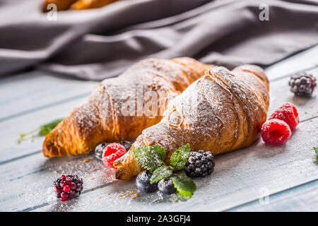 Freshly crispy croissants sprinkled sugar powder with raspberry blackberry and blueberry with mellisa leaves Stock Photo