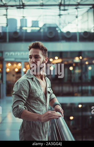 Young handsome man standing at the railing looking unsure or uneasy. Yearning for something as he looks back. Stock Photo