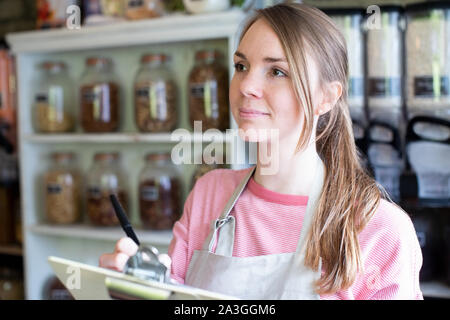 Female Owner Of Sustainable Plastic Free Grocery Store Checking Stock On Shelves Stock Photo