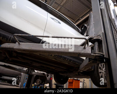 The car is hanging on a hydraulic lift in an auto repair shop. Above ...