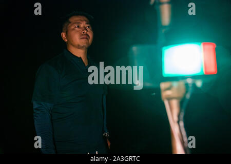 Takiya-ryo spearfishing. Fisherman Ikuya Yamamoto looks intently to the side at night, the green-and-white navigation light of his boat glowing sharply in the background on Lake Hamana near Hamamatsu, Japan. Stock Photo