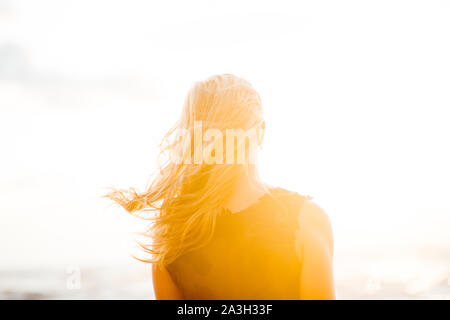 Beautiful young woman with golden blond curly hair outdoors at sunset with her back to us. Stock Photo