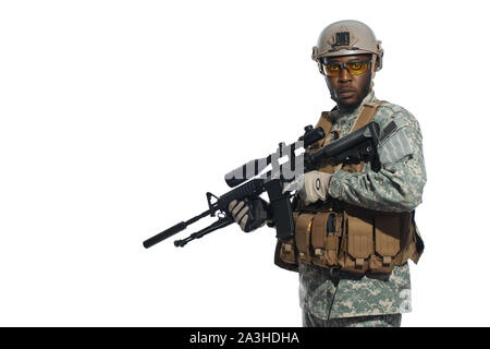 African male soldier wearing Americans army uniform and glasses protecting homeland. Man holding weapon machine in hands and looking at camera. White studio background. Stock Photo