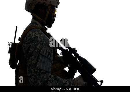 Silhouette of male soldier wearing Americans army uniform and helmet protecting homeland. Man holding weapon machine in hands and looking at side. White studio background. Stock Photo