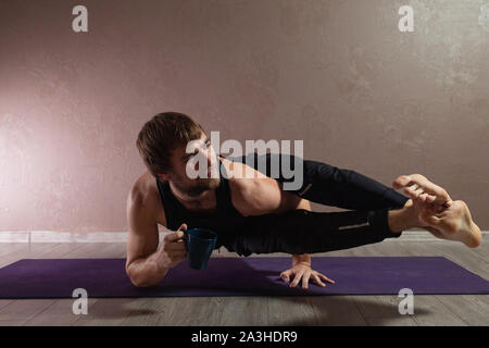 Young sporty man practicing yoga, meditating in yoga pose, working out, wearing sportswear, indoor full length, brown yoga studio Stock Photo
