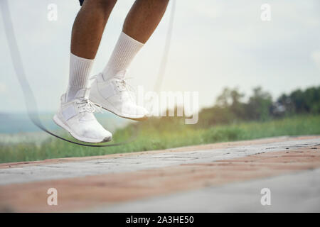 Close up of male feet in white socks and white sneakers on background of nature. Sportsman training with jumping rope, high jump. Stock Photo