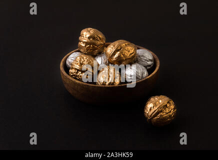 Painted golden and silver walnuts on wooden plate on black background Stock Photo